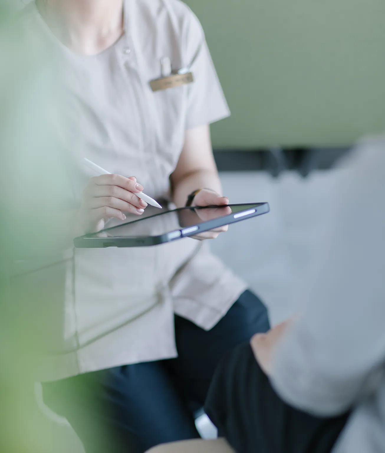 Healthcare professional in a light uniform using a tablet with a stylus in a calm setting.